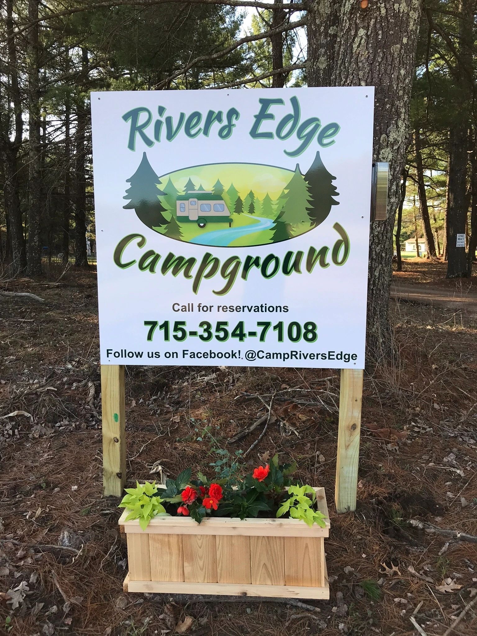 A sign for rivers edge campground is sitting in the middle of a forest.