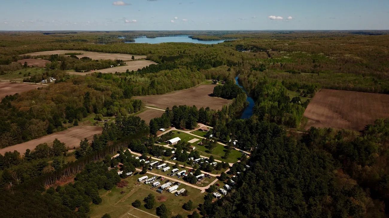 An aerial view of a campground surrounded by trees and fields with a lake in the background.