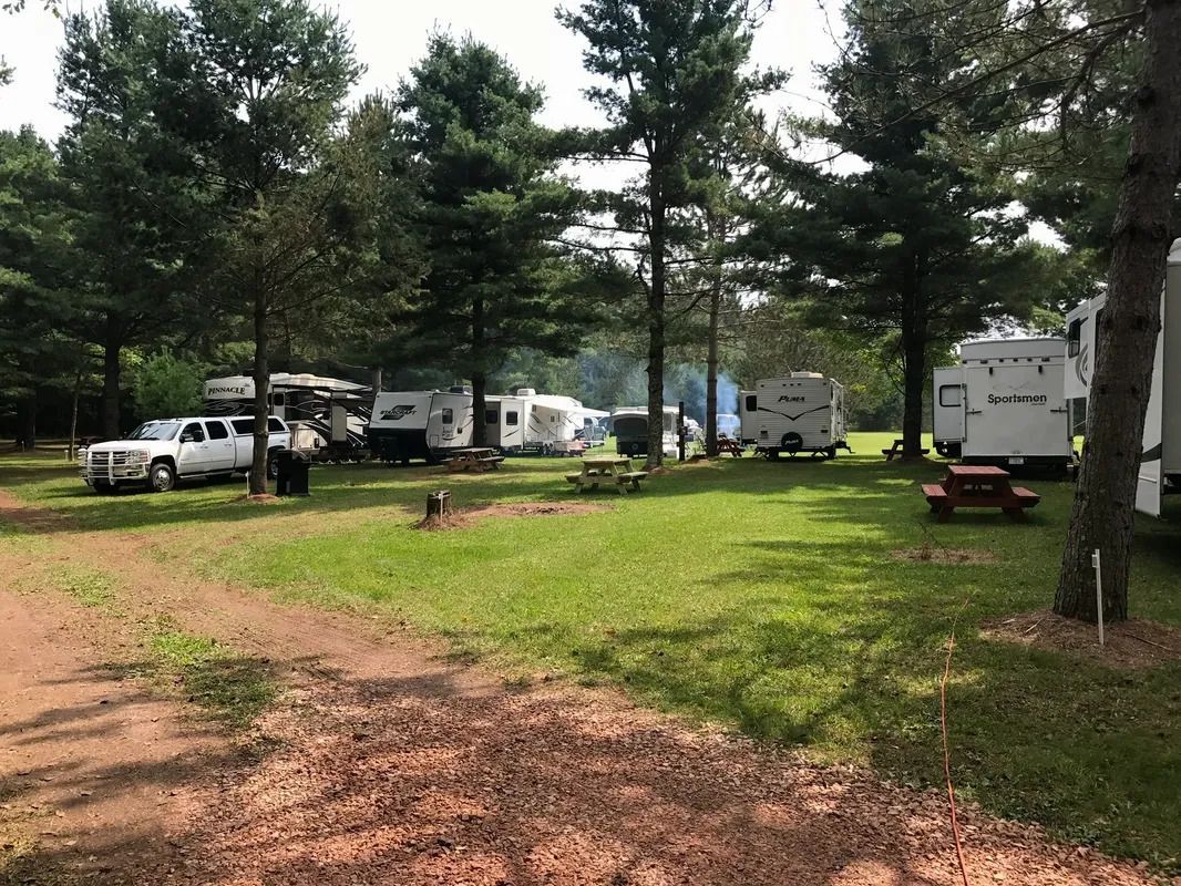 A group of rvs are parked in a grassy area surrounded by trees.