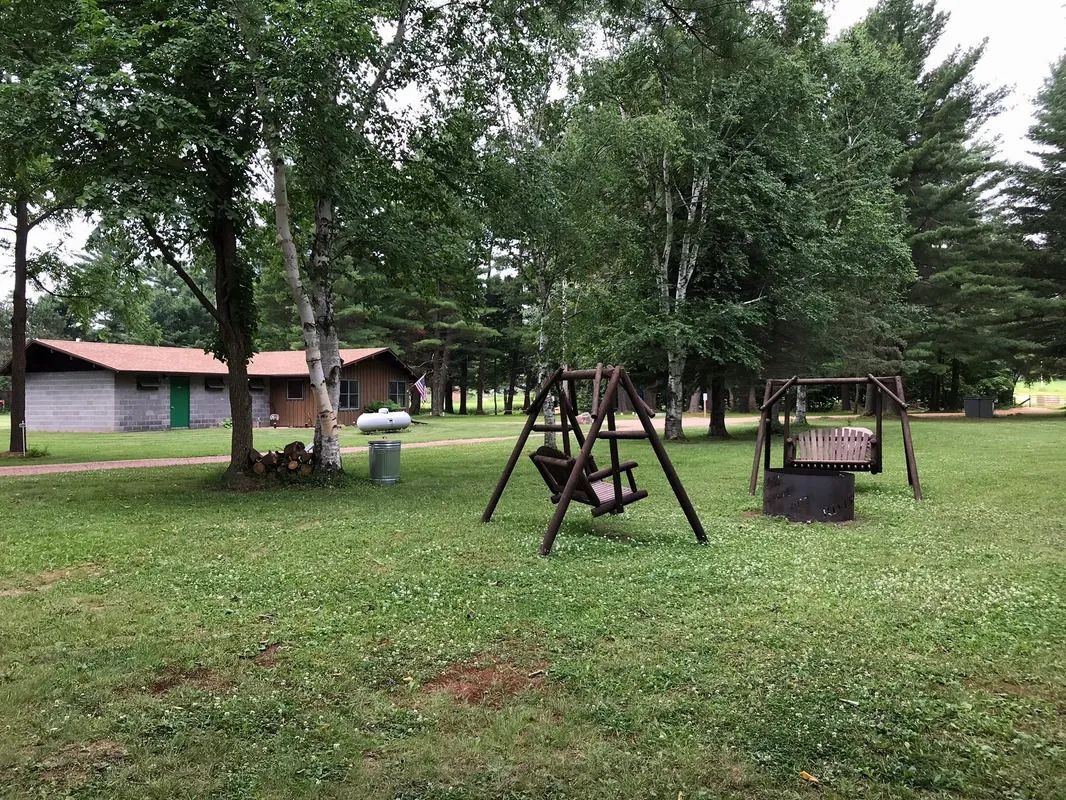 There are two swings in the middle of a grassy field.