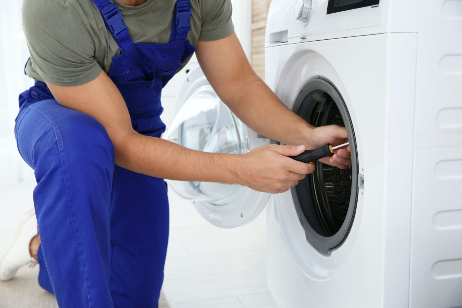A man is fixing a washing machine with a wrench.