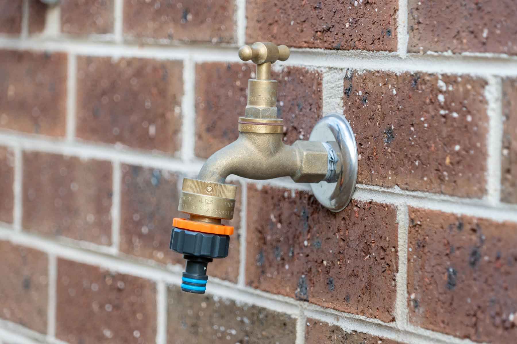 A brass faucet is attached to a brick wall.