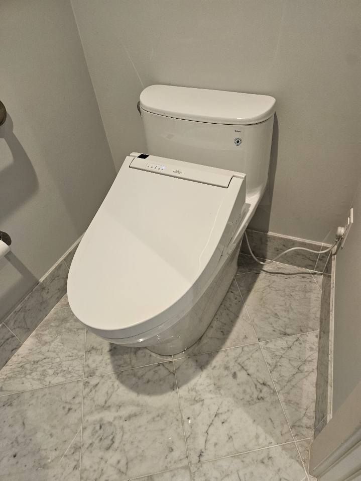 A white toilet is sitting on a marble floor in a bathroom.