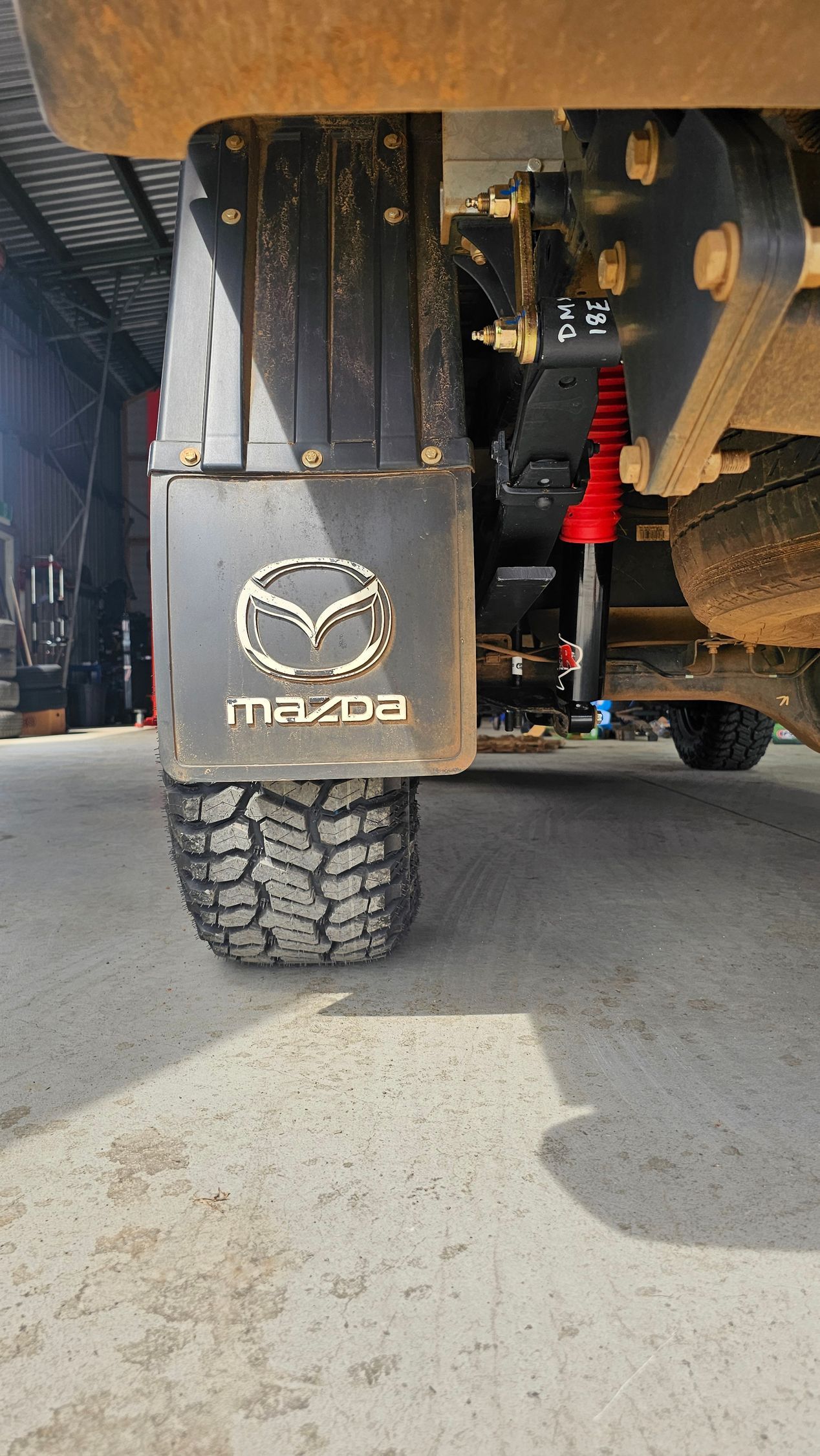 Mud flap with Mazda logo and off-road tire, showing rear suspension of a vehicle.