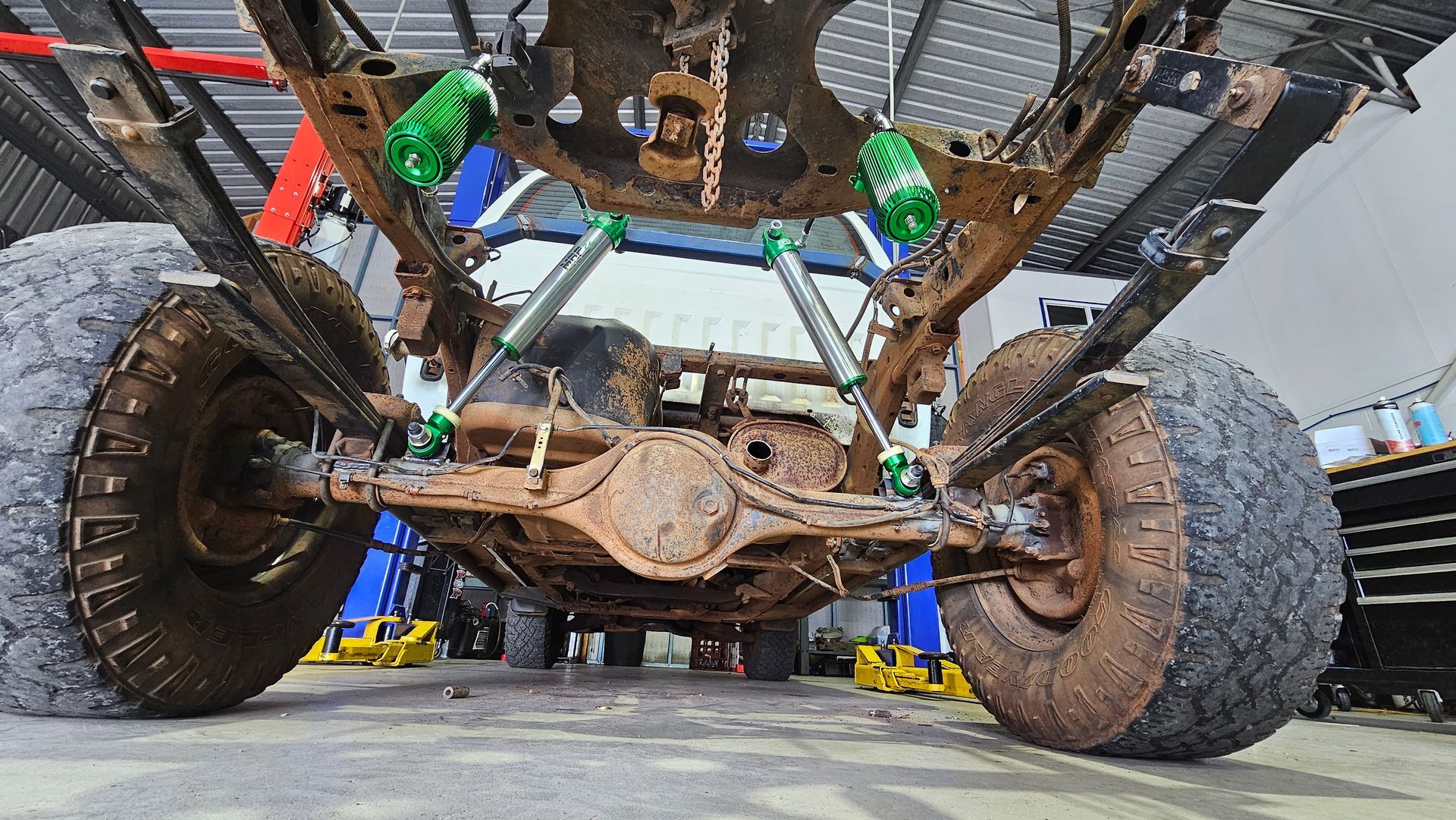 Underside view of a rusty 4x4 truck chassis with mud-covered tires and green shock absorbers — Track N Back 4x4 In Mareeba, QLD