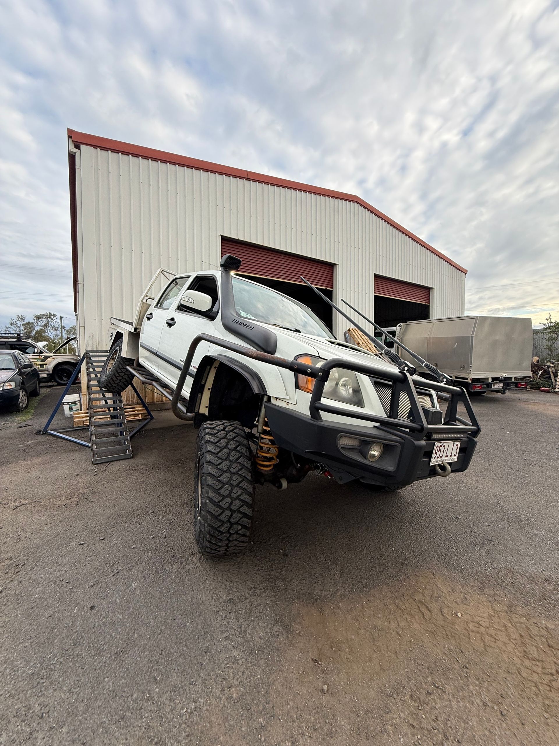 White lifted truck parked outside a red and white building, angled upward — Track N Back 4x4 In Mareeba, QLD