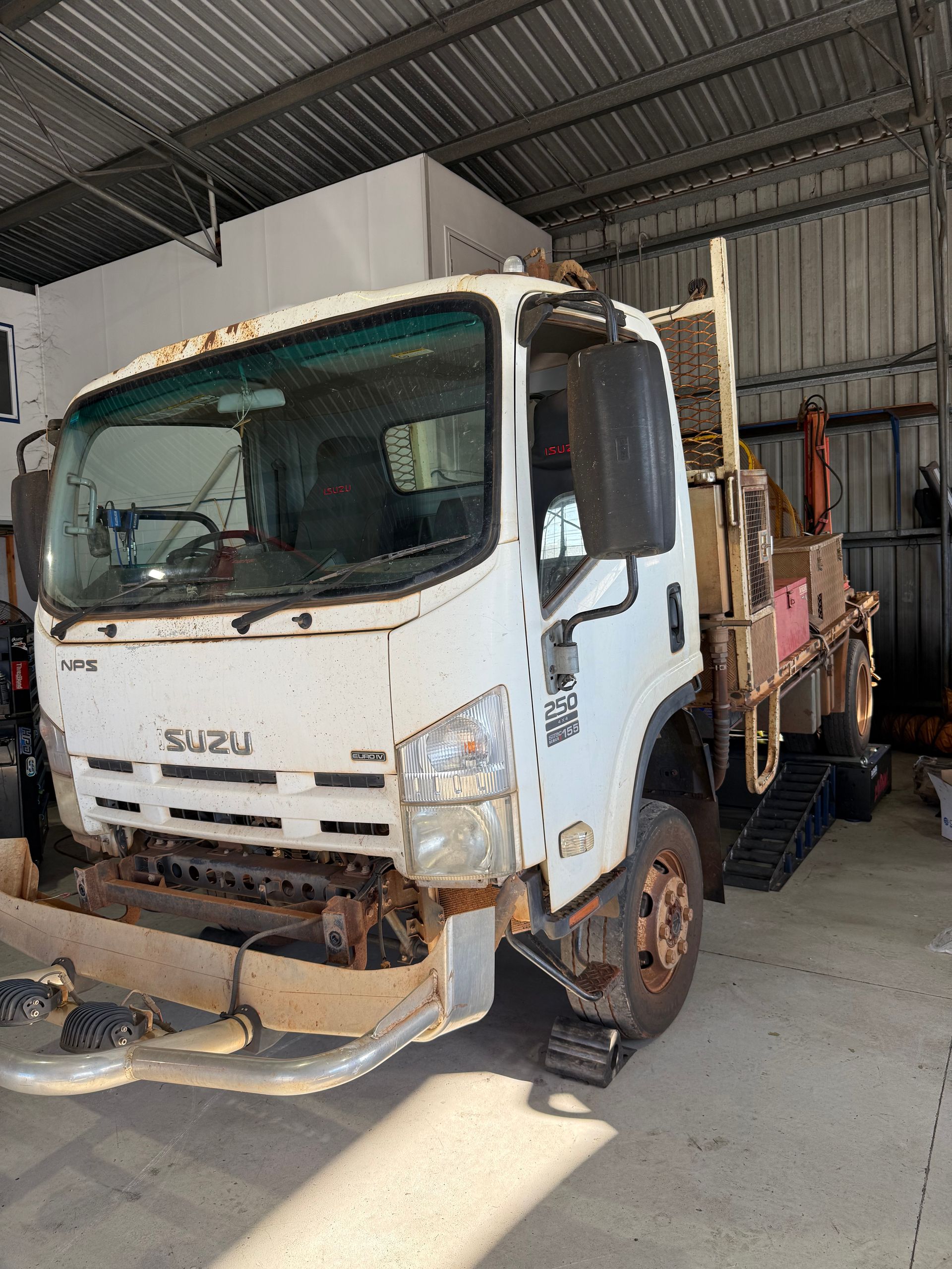 White Isuzu work truck in a garage; front is damaged, rust on the bumper and windshield — Track N Back 4x4 In Mareeba, QLD