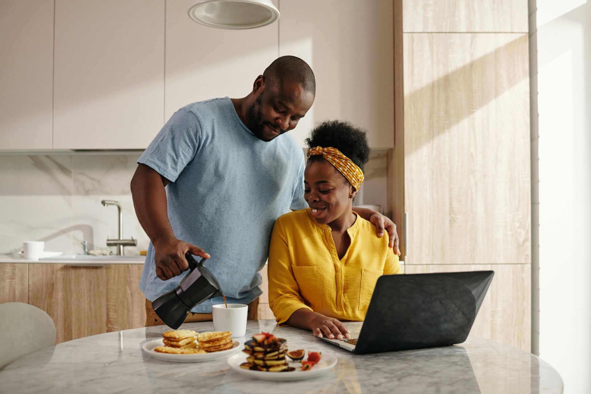 A man is pouring coffee into a cup while a woman is using a laptop.