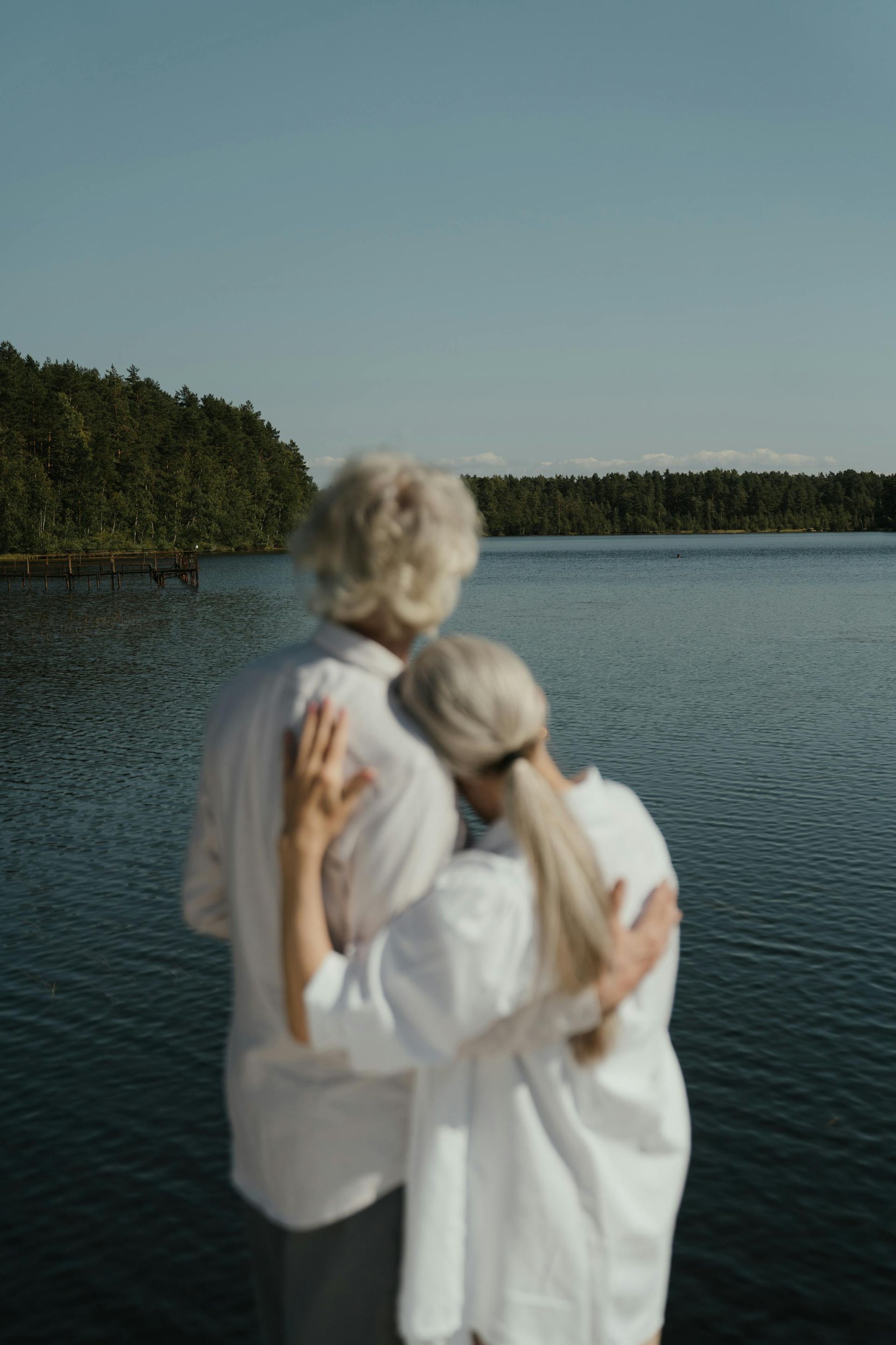 A man and a woman are hugging each other while standing next to a lake.