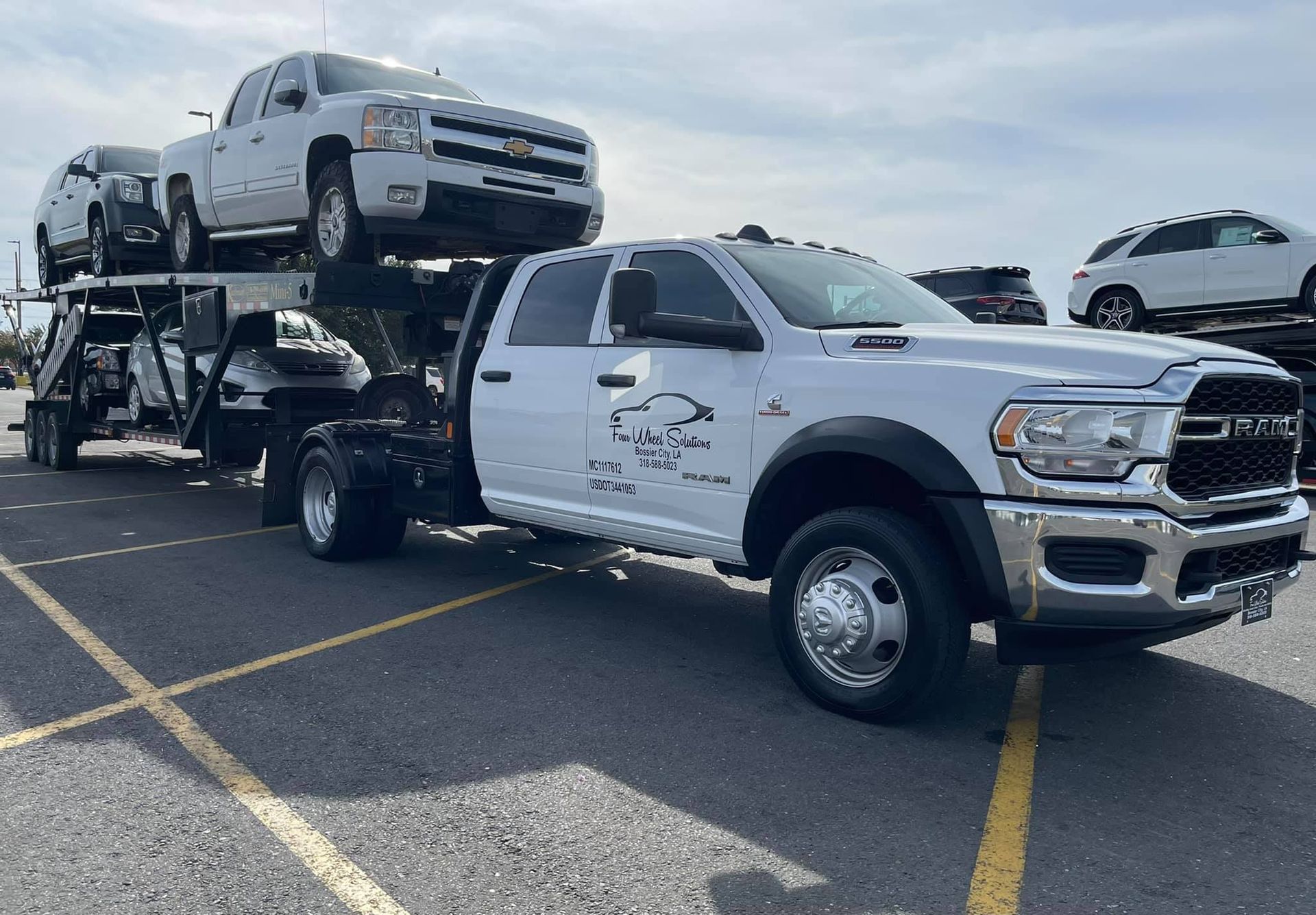A white tow truck is carrying two cars on top of it.