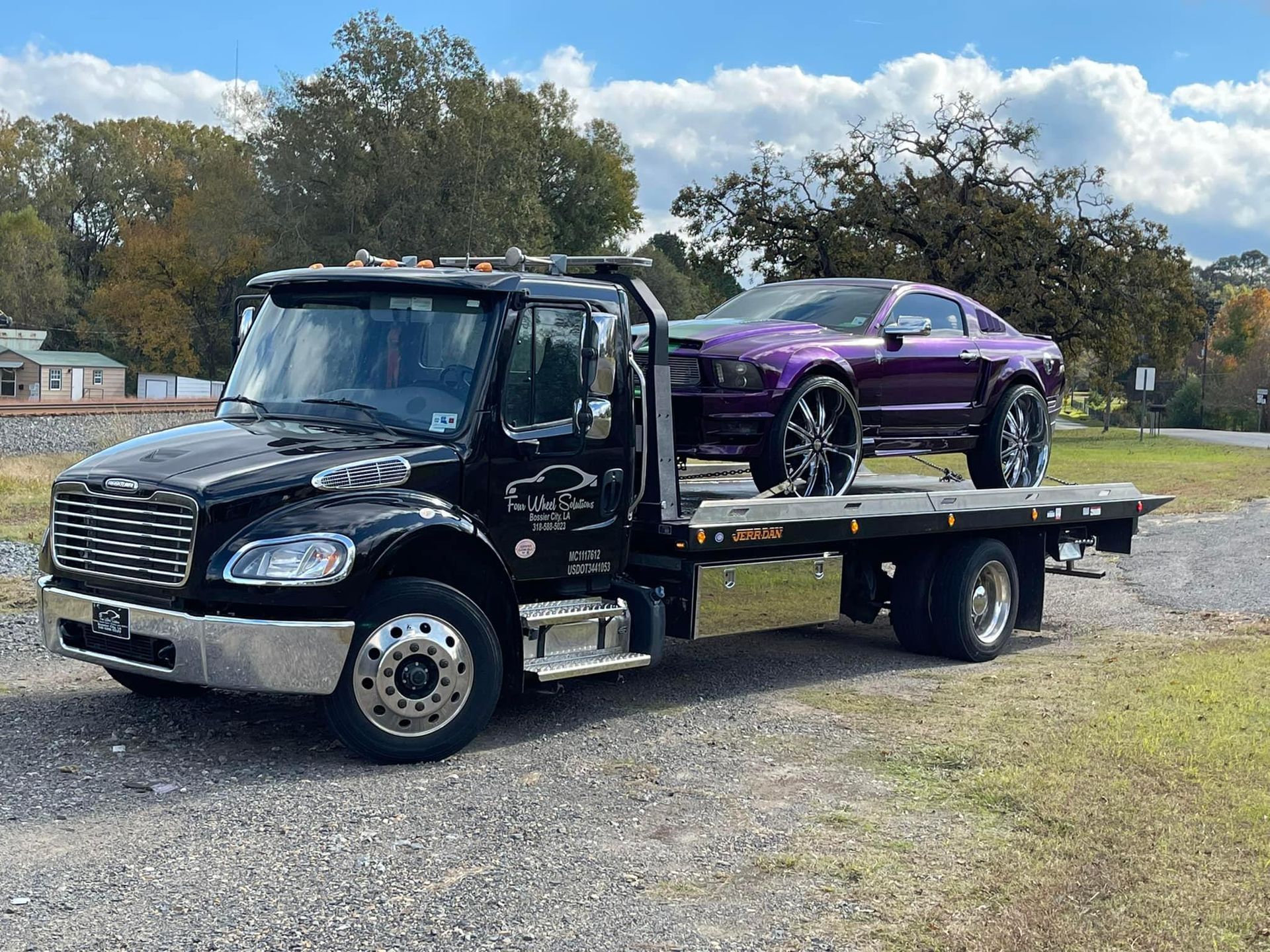 A black tow truck with a purple car on the back of it.