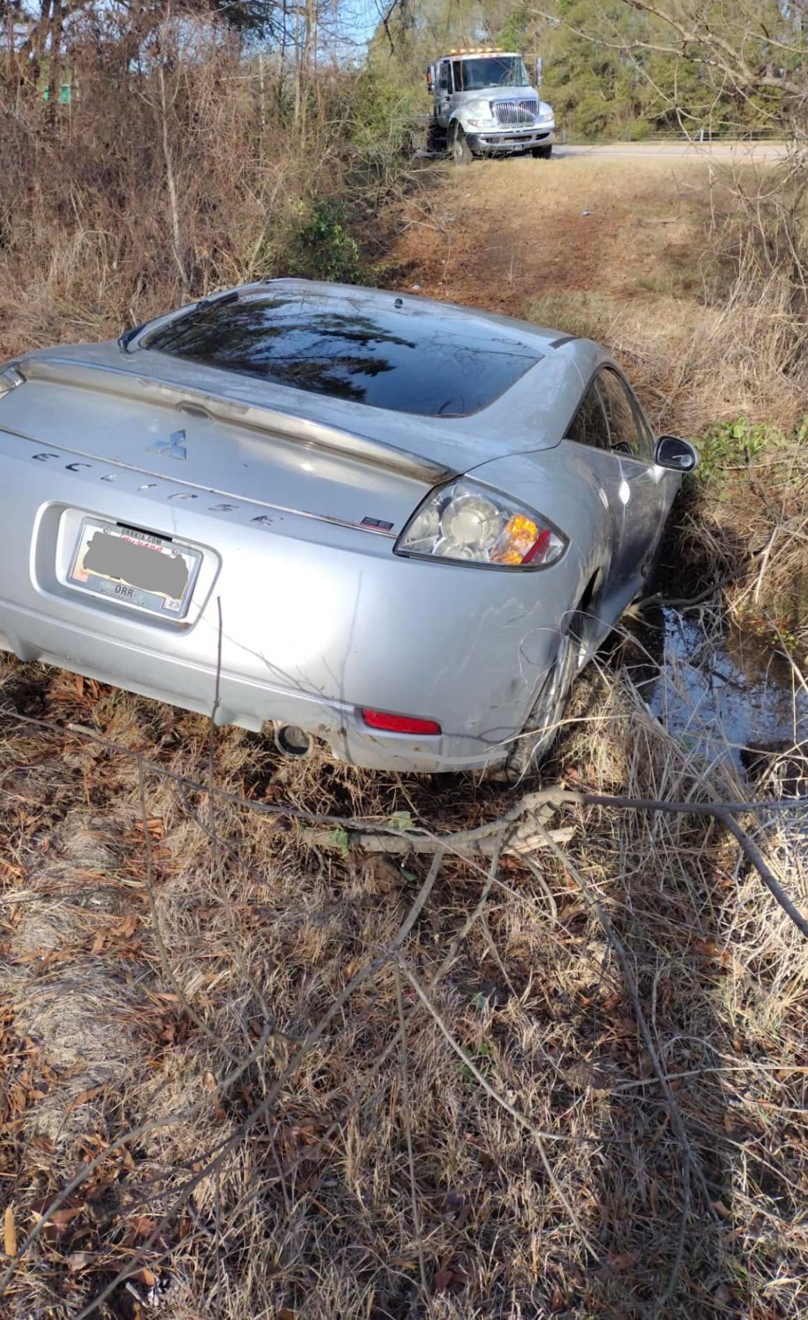 A silver car is stuck in the mud on the side of a dirt road.