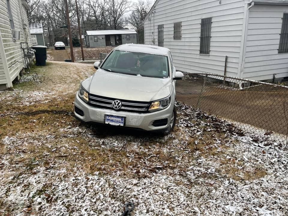 A silver volkswagen tiguan is parked in a snowy yard in front of a house.
