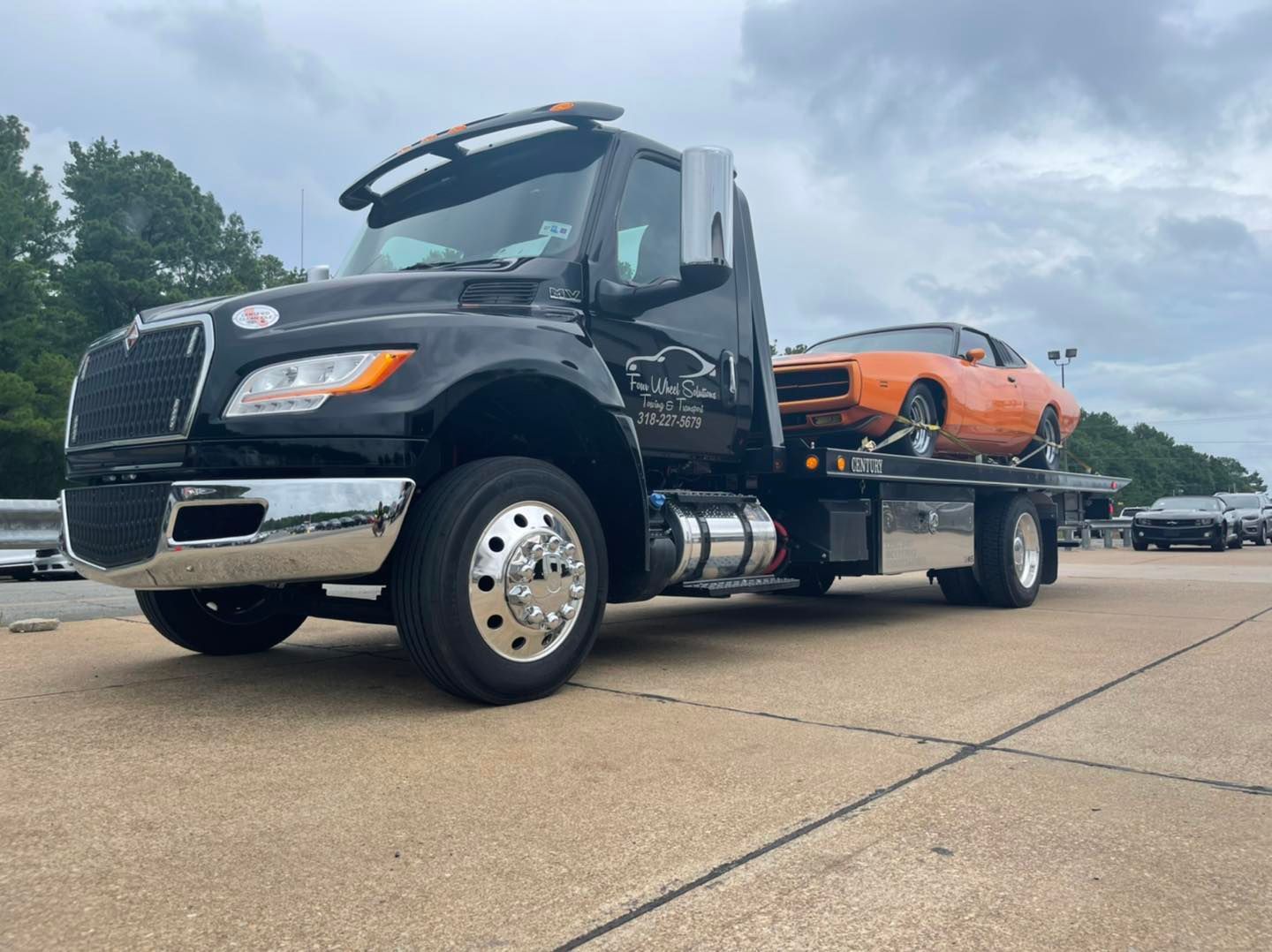 A tow truck with a car on the back is parked on the side of the road.