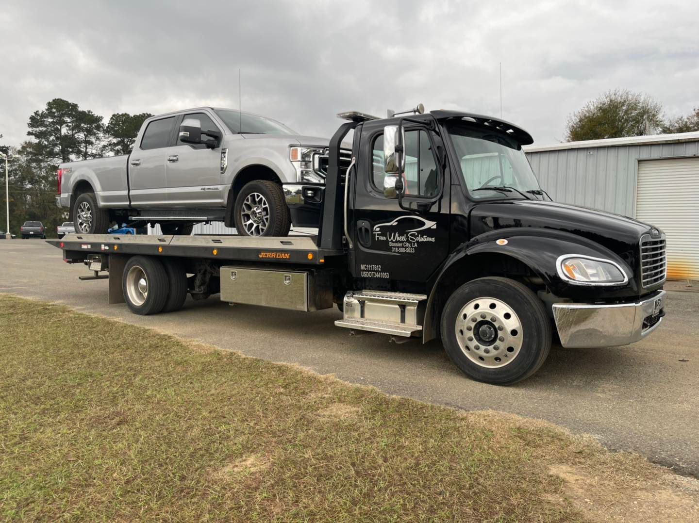 A tow truck is carrying a silver truck on the back of it.