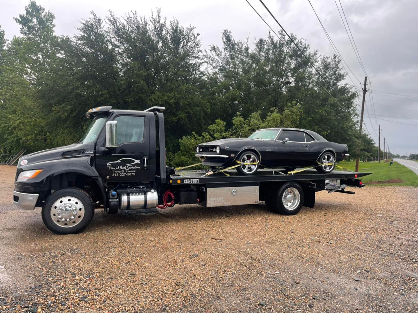 A tow truck is carrying a black car on the back of it.