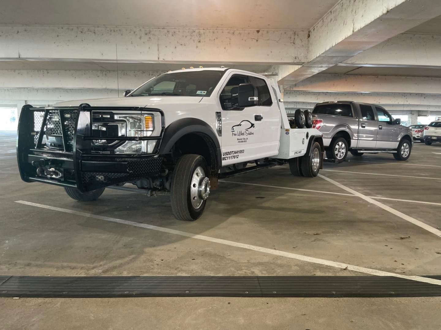 A tow truck is towing another truck in a parking garage.