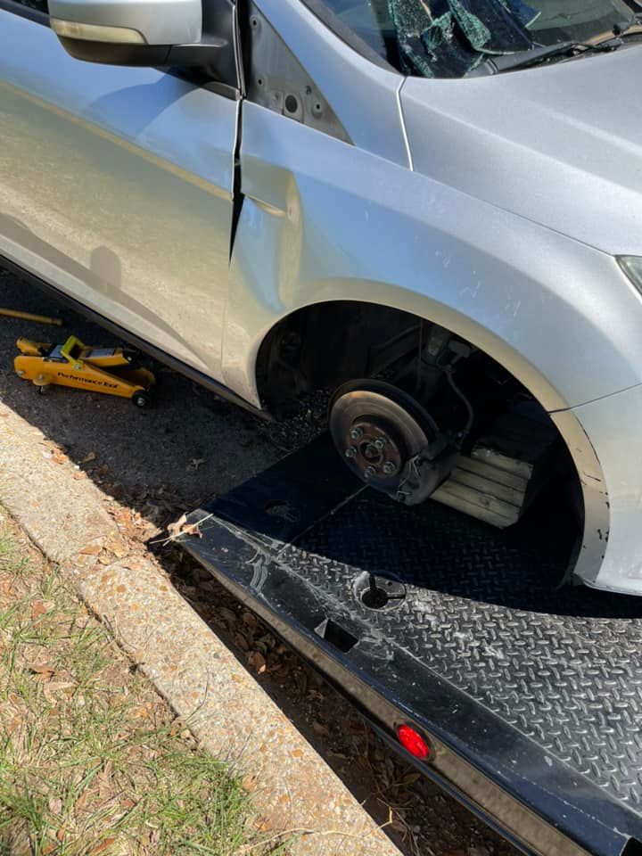 A silver car with a broken wheel is on a tow truck.