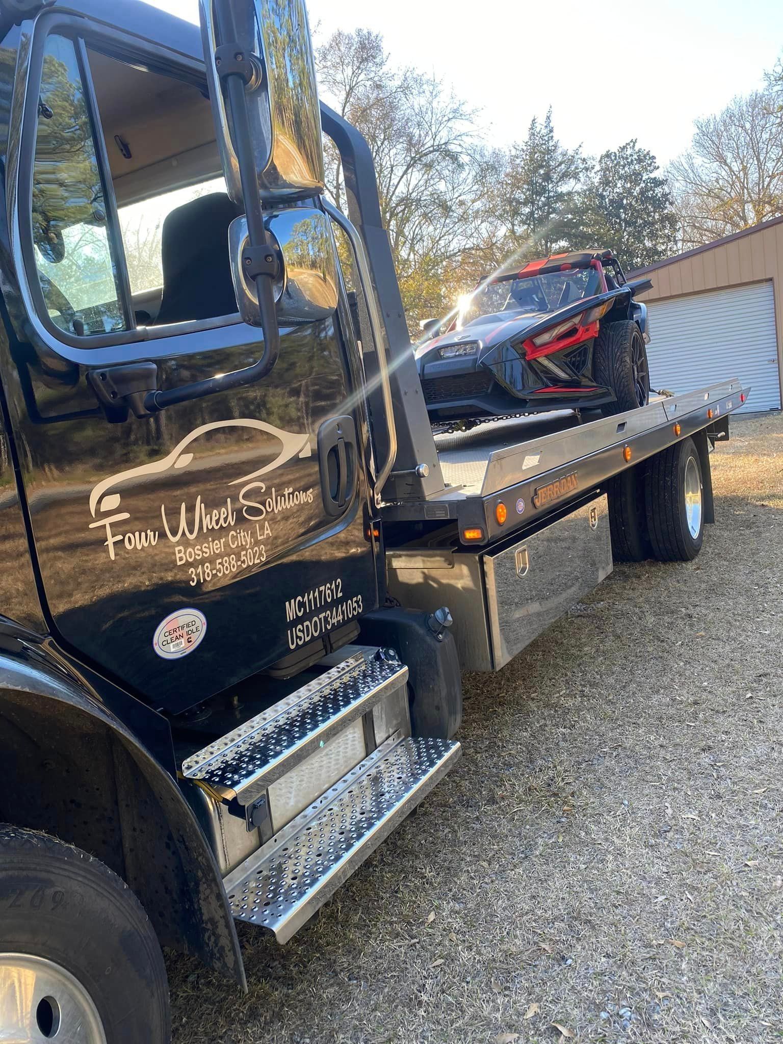 A black tow truck with a motorcycle on the back of it.