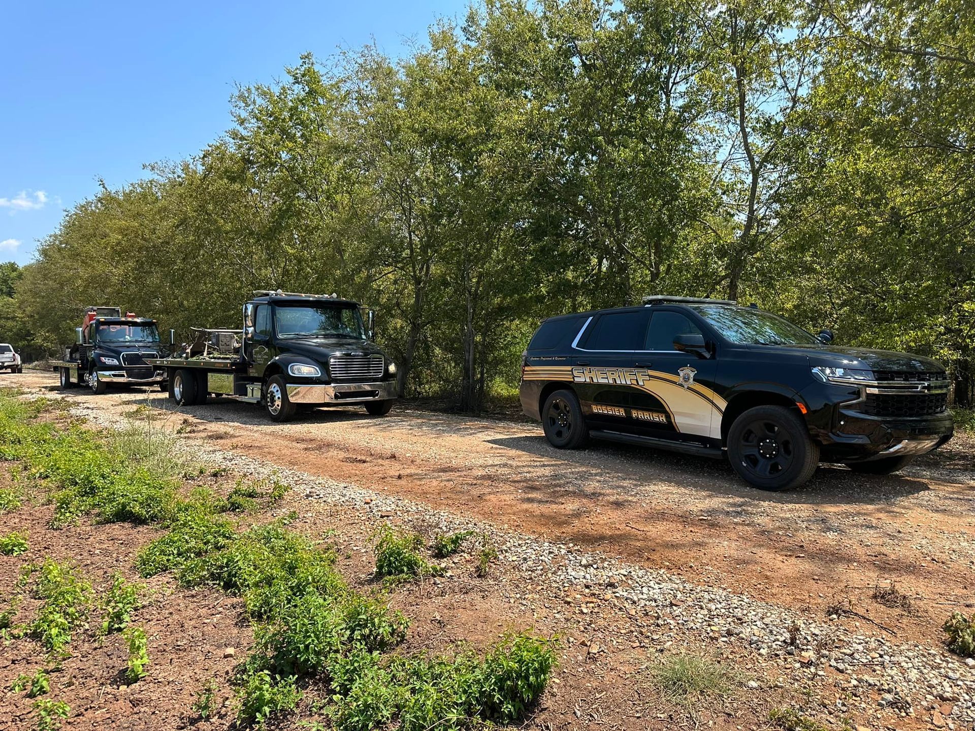 A row of tow trucks and a police car are parked on a dirt road.