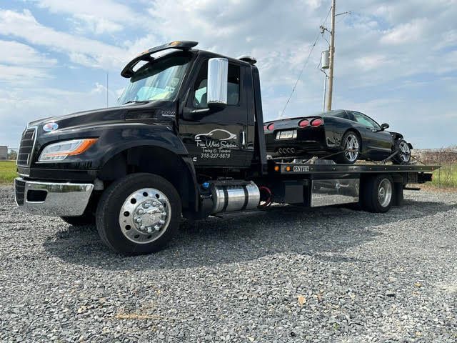 A black tow truck is towing a black sports car.