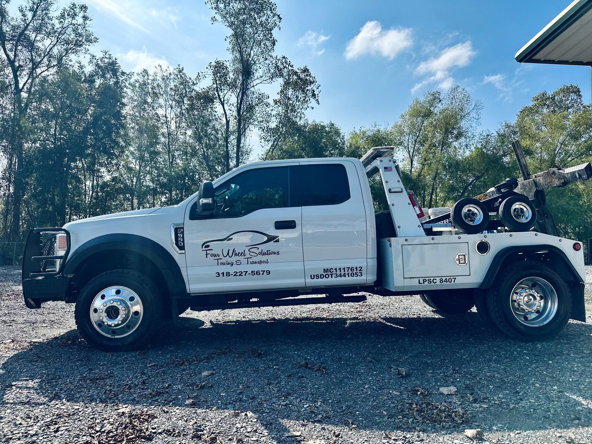 A white tow truck is parked in a gravel lot.