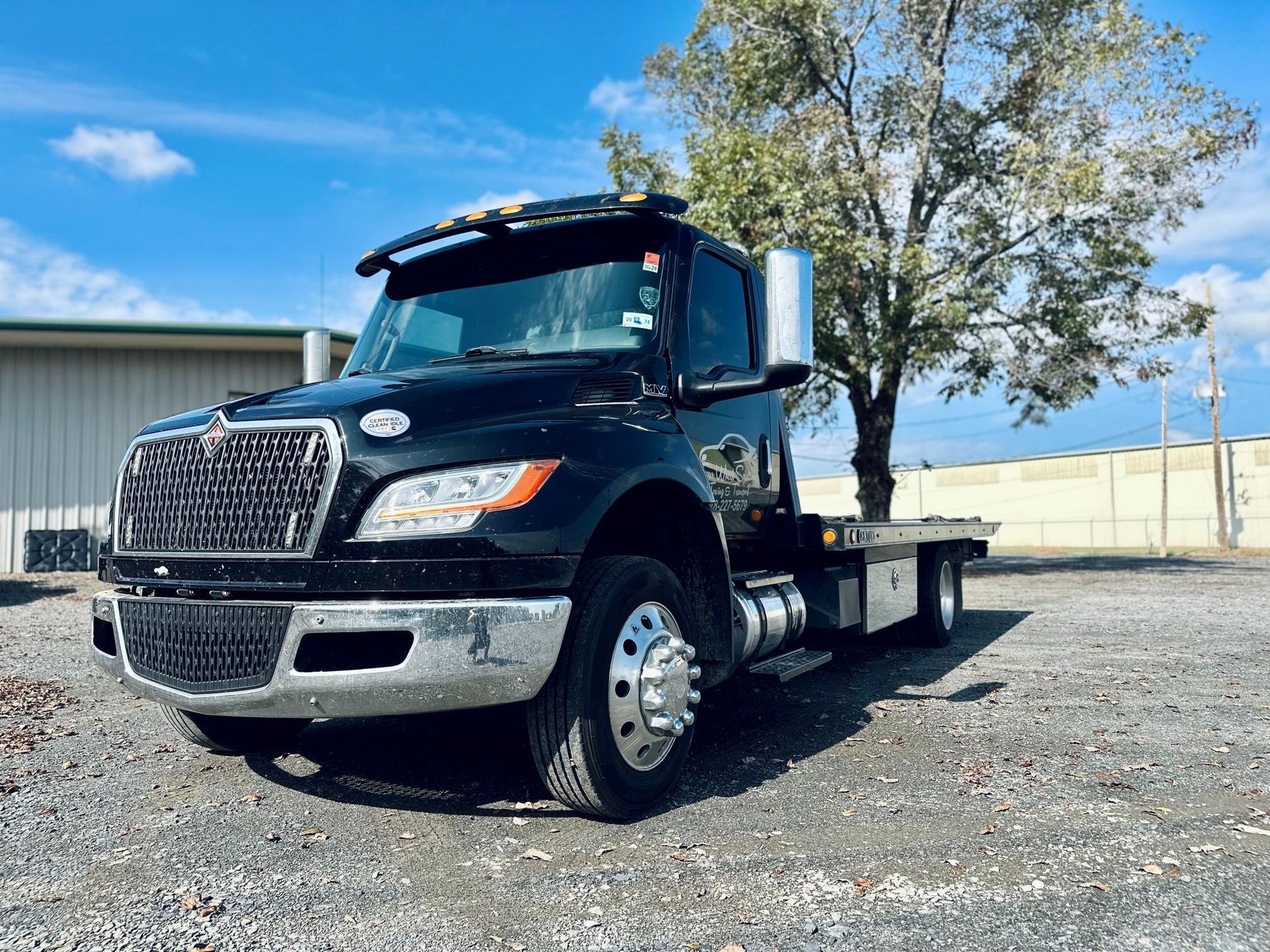 A black tow truck is parked in a gravel lot in front of a building.