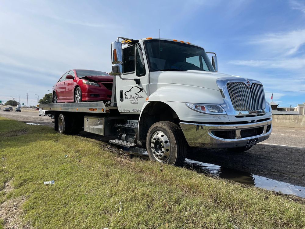 A tow truck is carrying a red car on the back of it.