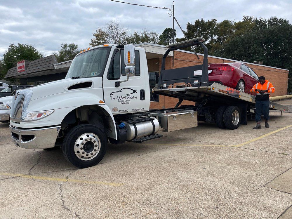 A tow truck with a red car on the back is parked in a parking lot.