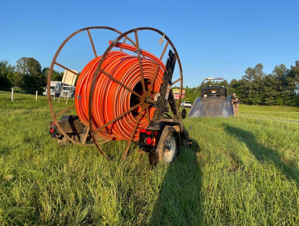 A large orange hose is on a trailer in a grassy field.