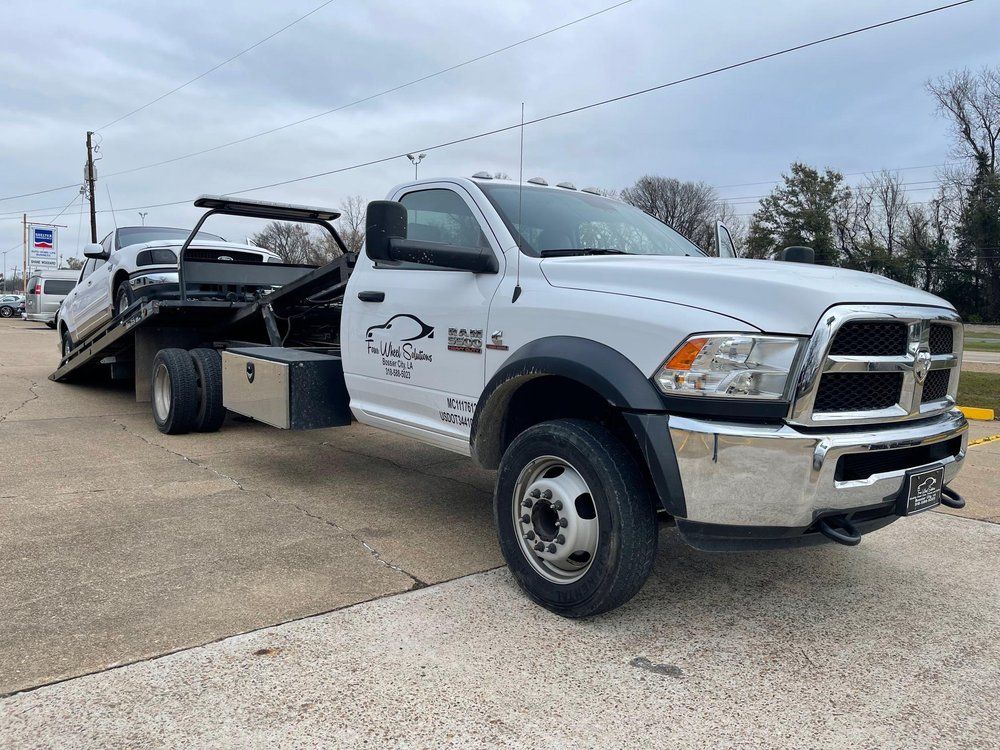 A white tow truck with a white car on the back is parked on the side of the road.