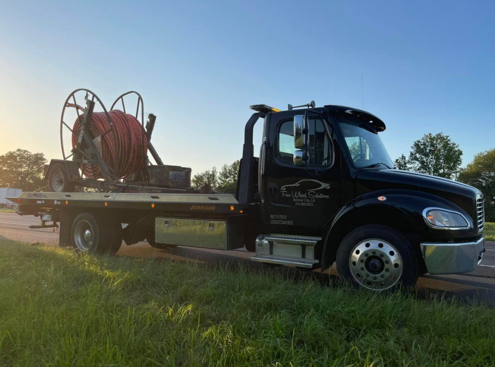 A black tow truck with a large hose on the back is parked in a grassy field.