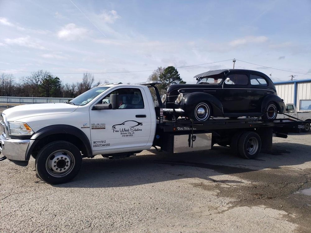 A tow truck is carrying a black car on the back of it.