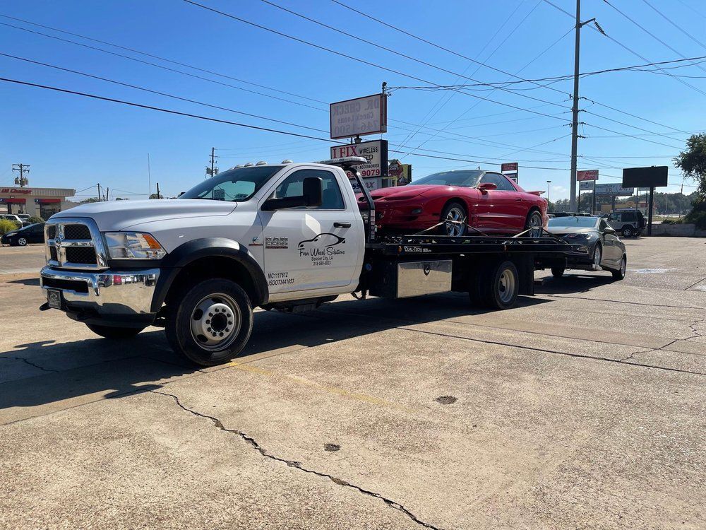 A tow truck is towing a red sports car in a parking lot.