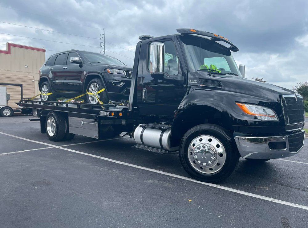 A black tow truck with a suv on the back is parked in a parking lot.