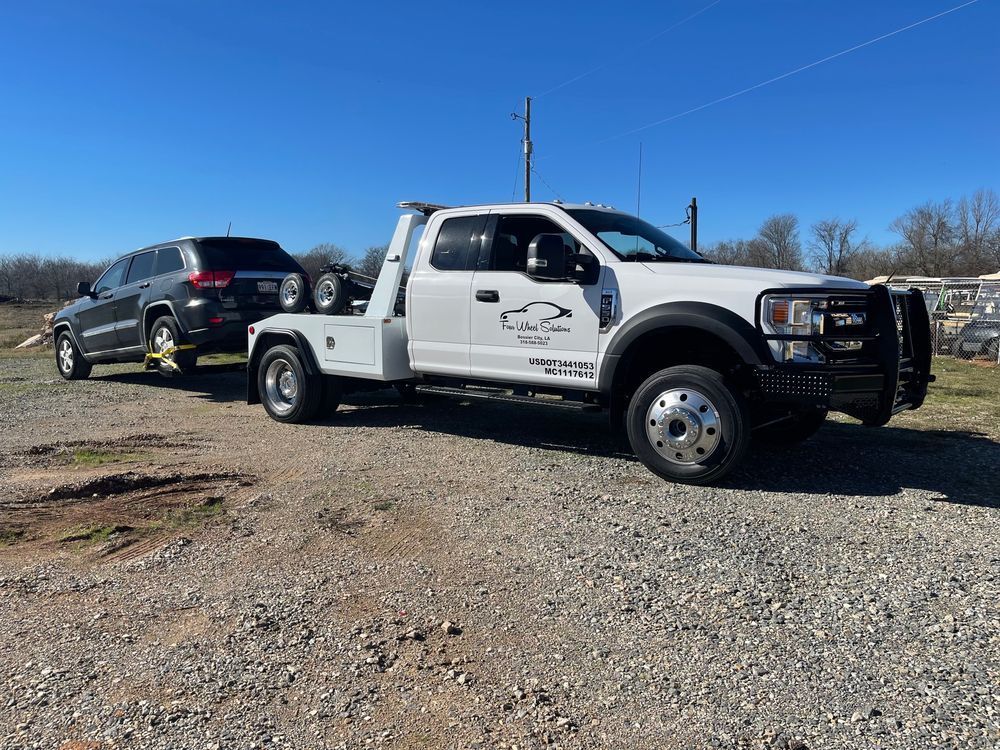 A white tow truck is parked next to a black suv in a gravel lot.