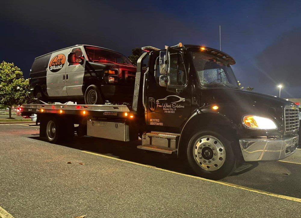 A tow truck is towing a police van in a parking lot at night.
