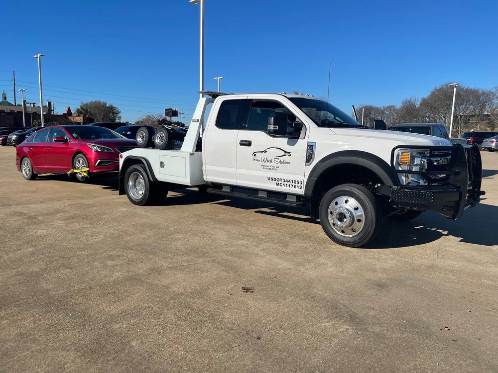 A white tow truck is towing a red car in a parking lot.