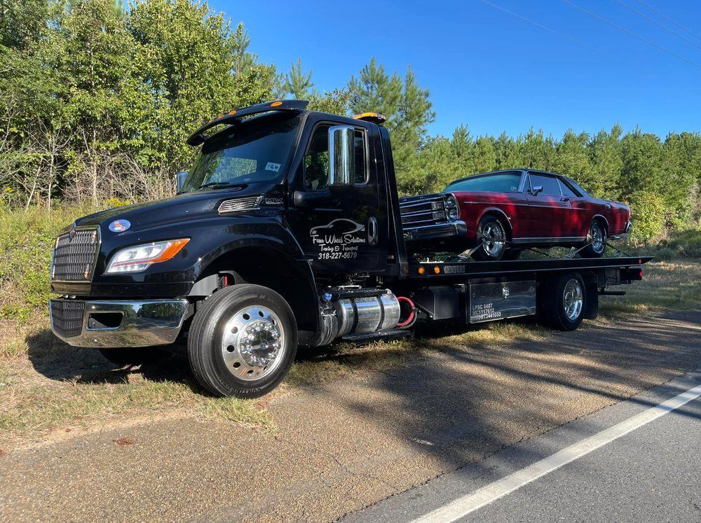 A tow truck is carrying a red car on the back of it.