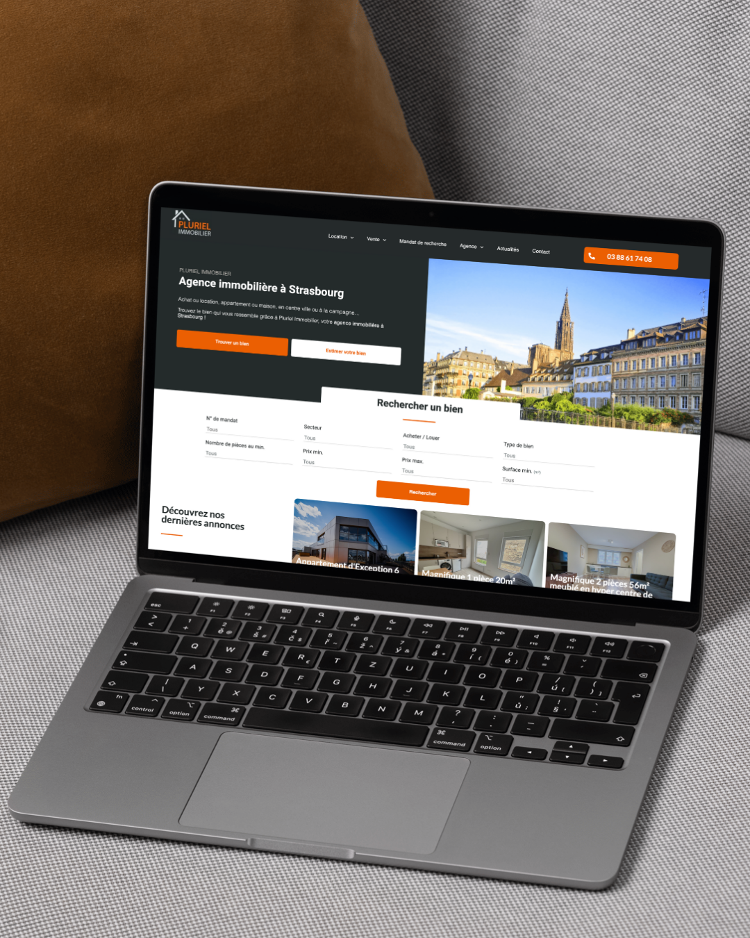 Ordinateur portable affichant un site Web de location d'appartements, avec une photo d'une ville et des accents orange.