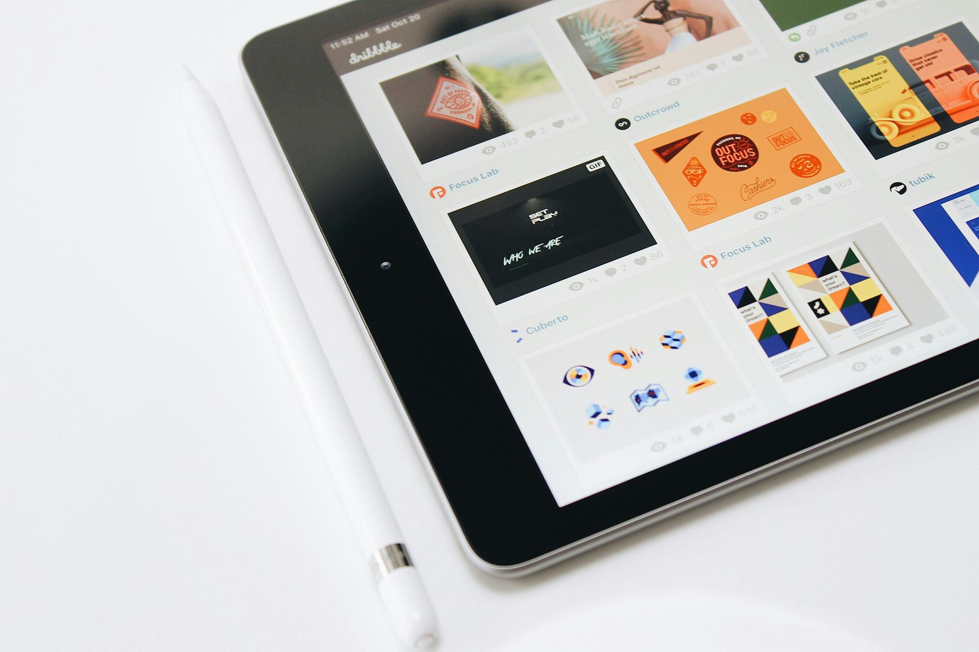 Tablette affichant une grille d'images de design, avec un stylet blanc sur une surface blanche.