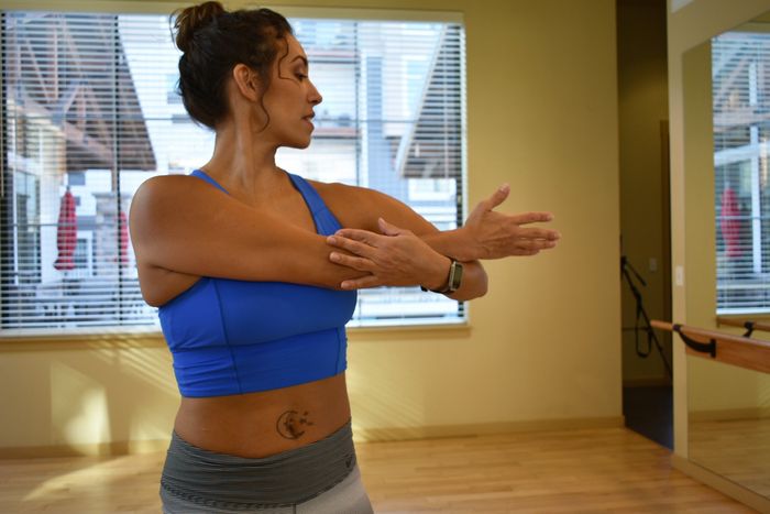 Alta doing an arm stretch while looking in a mirror