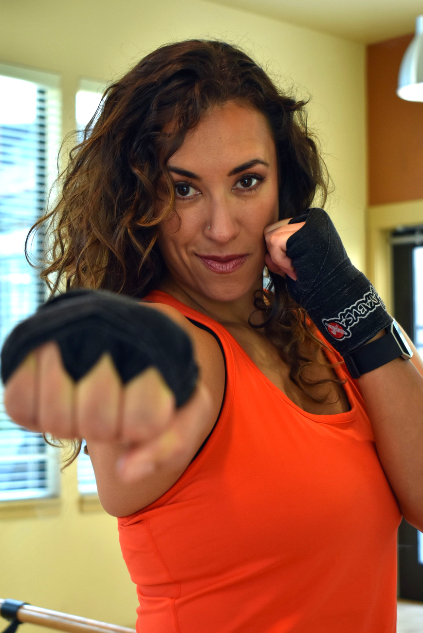 Fitness trainer Alta smiling, wearing an orange tank and throwing a punch toward the camera.