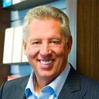 Man smiling, wearing a blue shirt and pinstripe suit, in an office setting.