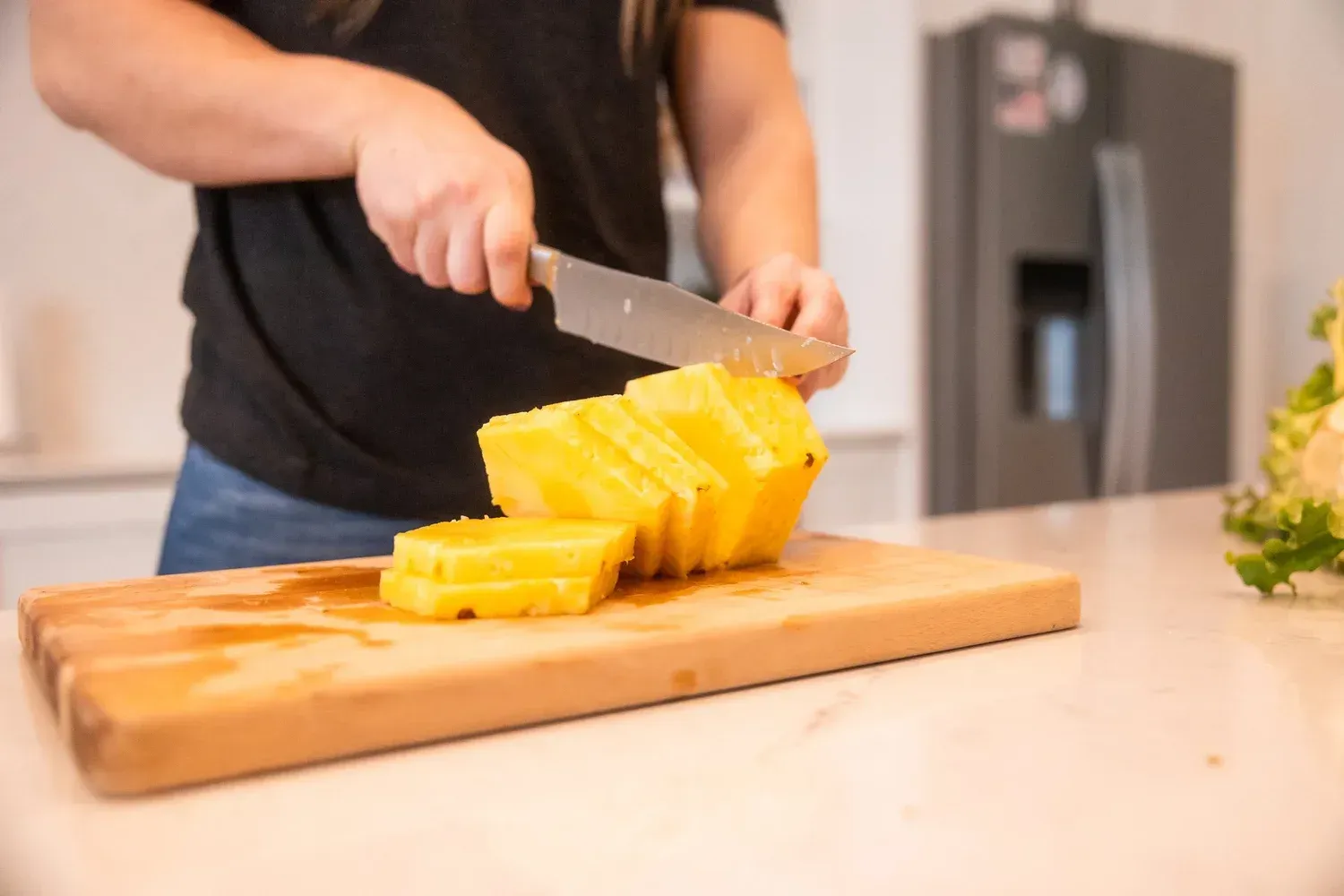 Person slicing pineapple on a wooden cutting board in a kitchen.