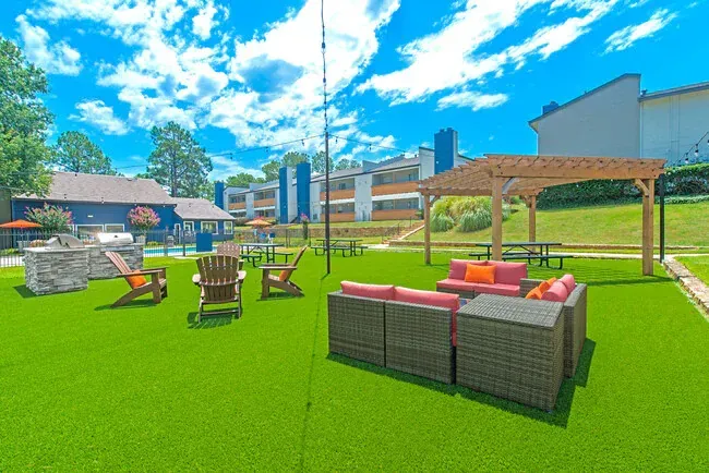 Outdoor patio area with seating, grill, and pergola on green turf under a blue sky.