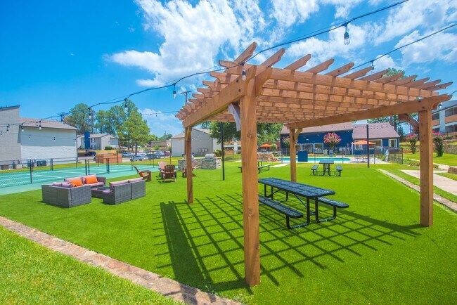 Wooden pergola over picnic table and artificial turf in outdoor recreation area.