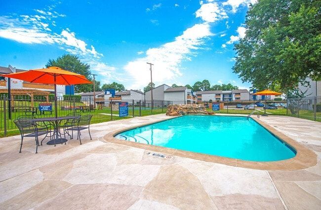 Pool area with orange umbrellas, tables, and blue water under a bright sky.