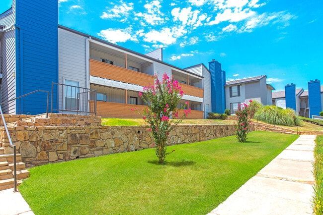 Apartment building with blue accents, brick wall, lush green lawn, and a blue sky.