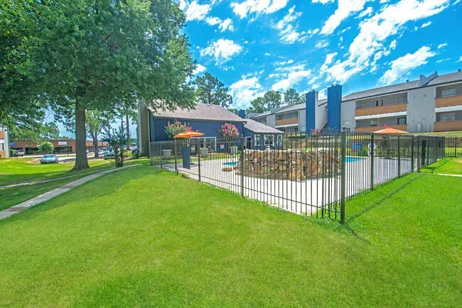 Lush green lawn and pool area fenced off from apartment buildings with blue accent colors under a blue sky.
